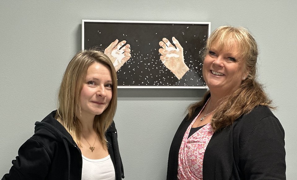 Ett fotografi på två kvinnor framför en tavla som illustrerar två händer. 